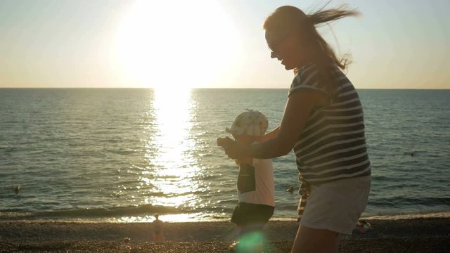 Young mother walking with cute baby on the oceanfront at sunset. The baby is still very poor, and my mother runs it holds. The concept of the first steps in life