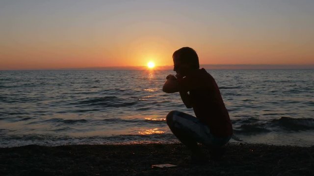Silhouette man with smartwatch on hand at sunset beach. He touches the smart watches and checks the message. The sun is almost set behind the ocean.