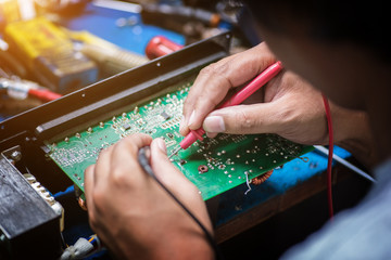 Technician repairing a television. Hand with voltmeter above board with components. Repair of circuits electric equipment, close up