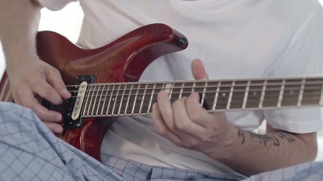Closeup of hands of man sitting in pajamas and playing the guitar 