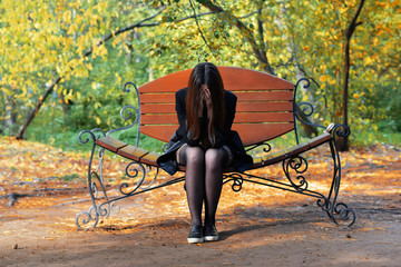 Girl sitting on the bench, covering face with his hands
