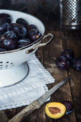 Pflaumen in einem Lochsieb und einem Messer auf einem alten rustikalen Holzuntergrund