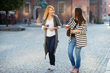 Two attractive girls tourists walk the streets of the old town with a coffee in hand.