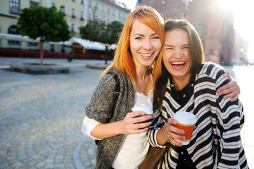 Two cute young women standing on the square of the beautiful European city.