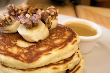 Pancakes topped with sliced bananas and pecans and maple butter