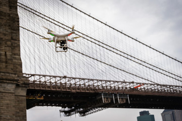 White drone flying in New York City on a cloudy day with Brooklyn Bridge in background