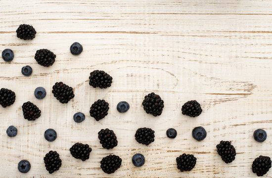 Blackberries and blueberries in a corner of the frame on a white wooden board, with space for text