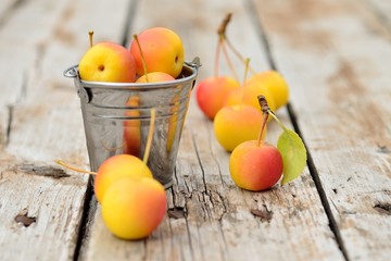 Little apples on a wooden table and a small metal bucket. Selective focus