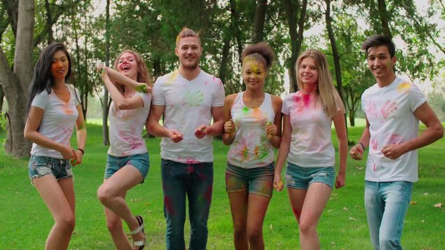 Multi-ethnic Group celebrate Holi festival in the Park , all in bright colours, look and shoot paint at camera in the Park, slow motion
