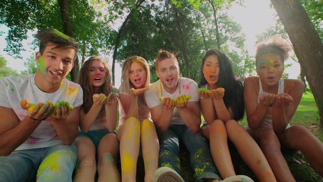 Multi-ethnic Group celebrate Holi festival in the Park , all in bright colours, look and blow at the camera in the Park, slow motion