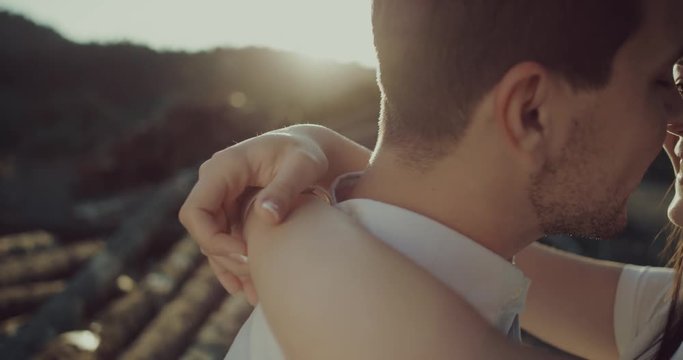  Lovers man and woman rubbing noses against each other at sunset and smiling near a pile of logs in forest. Girl hugging her boyfriend.
