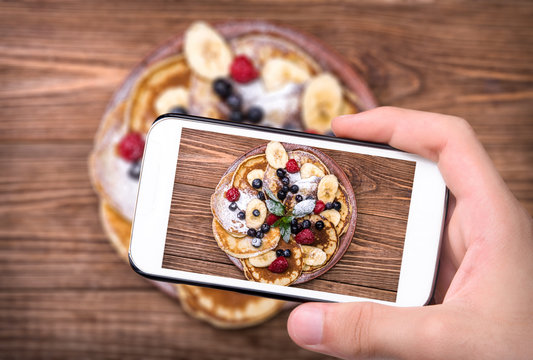 Hands taking photo pancakes with fresh fruit  with smartphone.