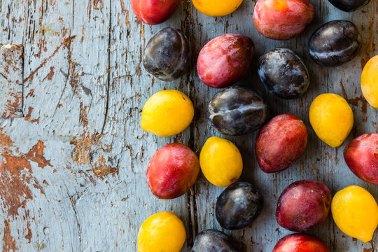 Organic red, blue and yellow plums on the blue wooden table. Dark rustic style, top view  