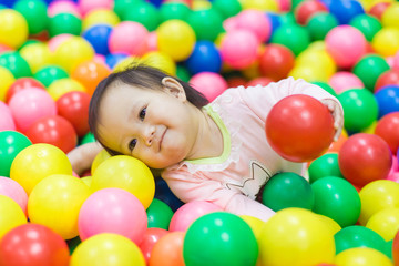 Fototapeta na wymiar An emotional face of smiling baby playing in the balls pool. Cute and happy girl.