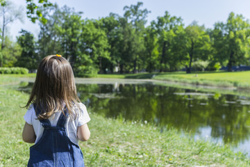 Adorable little girl standing by the water in the park