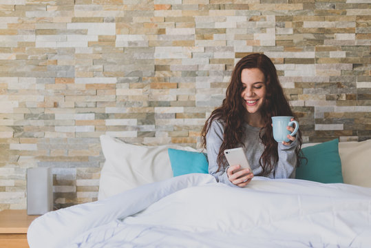 Peaceful ginger woman using mobile with cup of coffee in hand