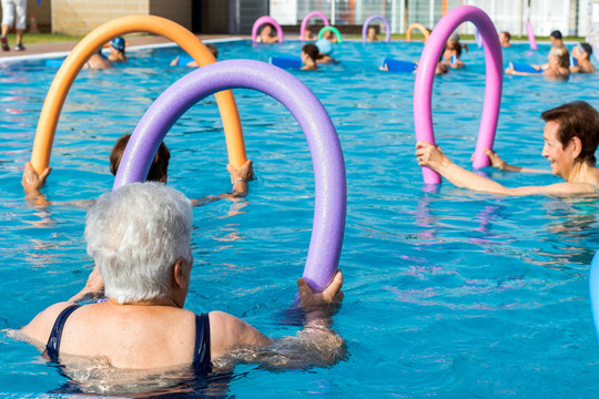 Senior women doing exercise with soft foam noodles in pool.