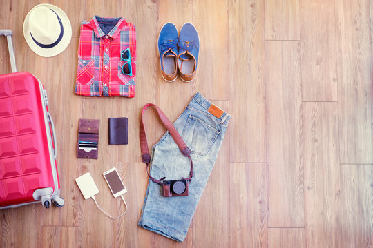 Ready for travel. Essentials for tourist. Different male clothes, accessories and gadgets on wooden floor. Valise, wallet, passport, smartphone and powerbank, shoes, camera, hat.