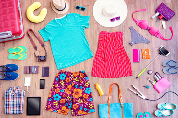 Ready for travel. Overhead of essentials for vacation. Top view of male and female summer accessories, clothes and gadgets on the wooden background. Packing suitcase.