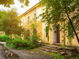 Fototapeta na wymiar Old facade in beautiful picturesque courtyard. Yellow building with arched windows and shabby walls in the background of green plants and leaves