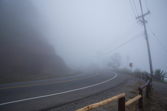 Misty curve road along the mountain in the morning with electric pole on the side way.