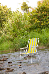 Alone yellow chair put in stream rocky waterfall with green environment forest nature background.