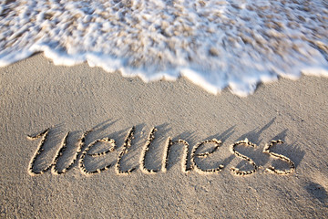 Wellness concept written on sand.