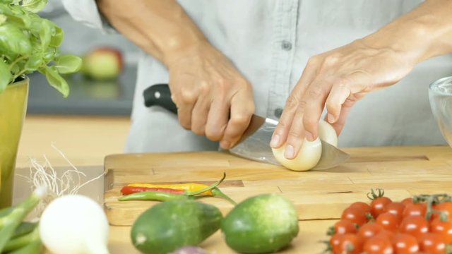 Woman taking onion and cutting it into slices on wooden board, dolly shot
