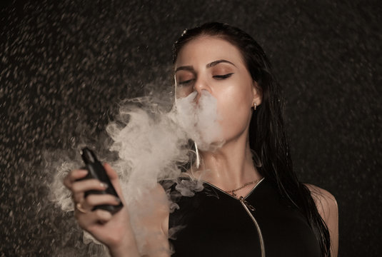Young beautiful woman vaping e-cigarette. Water flowing on lwoman face.