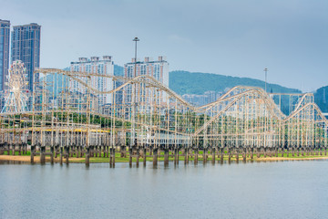Roller coaster steel structure built above a lake with background of skyscrapers
