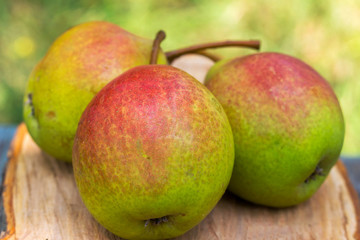 Three ripe organic pears on wooden board, blurred background, selective focus.