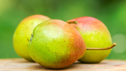 Three ripe organic pears on wooden board, blurred background, selective focus.