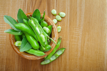 Bowl of podded green broad beans on a wooden table. Healthy organic food. Top view.