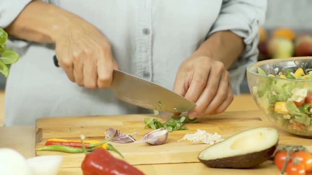 Woman hlding bunch of basil's leaves and cutting them on wooden board, dolly shot
