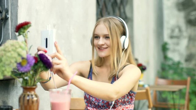Girl doing selfies on smartphone while listening music in the outdoor cafe
