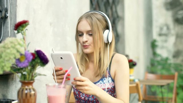 Girl connecting headphones to tablet and start listening music
