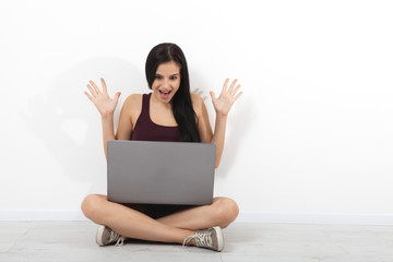Happy young woman sitting on floor with crossed legs and using laptop, talk on Skype on white...