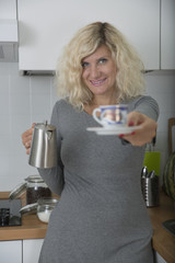 Blonde girl with curly hair is offering small cup of coffee