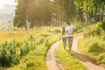 A view of a young couple walking near the forest holding each other waists and looking at each other gently