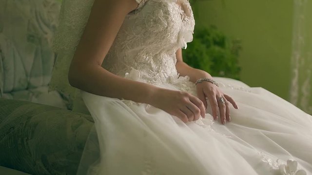 The beautiful amusing bride in a white dress sits on a brown background