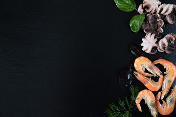 Preparing fresh seafood in the kitchen with gourmet pink shrimp and octopuses surrounded by fresh herbs and spices on black stone background