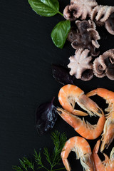 Preparing fresh seafood in the kitchen with gourmet pink shrimp and octopuses surrounded by fresh herbs and spices on black stone background