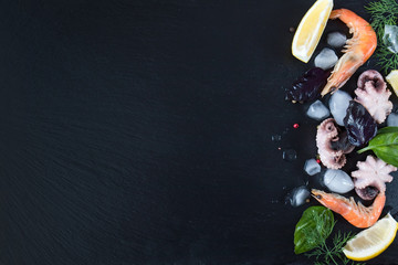 Verse zeevruchten bereiden in de keuken met gastronomische roze garnalen en octopussen omringd door ijs, verse kruiden en specerijen op zwarte stenen achtergrond