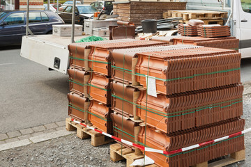 Dachziegel aus Ton auf Palette und ein Handwerker-Pritschenwagen