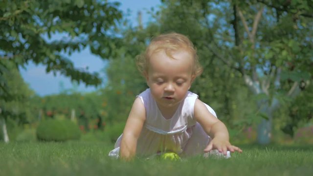 Baby putting green apple on the grass.
