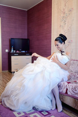 Fototapeta premium Beautiful bride in lingerie is watching a wedding dress. Beauty model girl in white clothes. Female portrait with bridal gown for marriage. Woman with curly hair and lace veil. Cute lady indoors