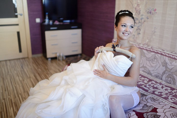 Fototapeta na wymiar Beautiful bride in lingerie is watching a wedding dress. Beauty model girl in white clothes. Female portrait with bridal gown for marriage. Woman with curly hair and lace veil. Cute lady indoors
