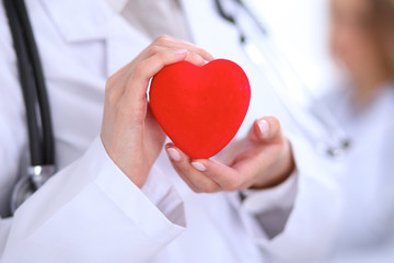 Female doctor with stethoscope holding heart.  Patients couple sitting in the background