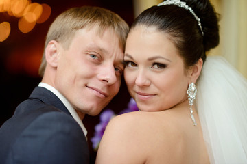 Wedding couple indoors is hugging each other. Beautiful model girl in white dress. Man in suit. Beauty bride with groom. Female and male portrait. Woman with lace veil. Cute lady and handsome guy