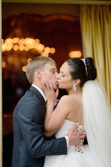 Wedding couple indoors is hugging each other. Beautiful model girl in white dress. Man in suit. Beauty bride with groom. Female and male portrait. Woman with lace veil. Cute lady and handsome guy